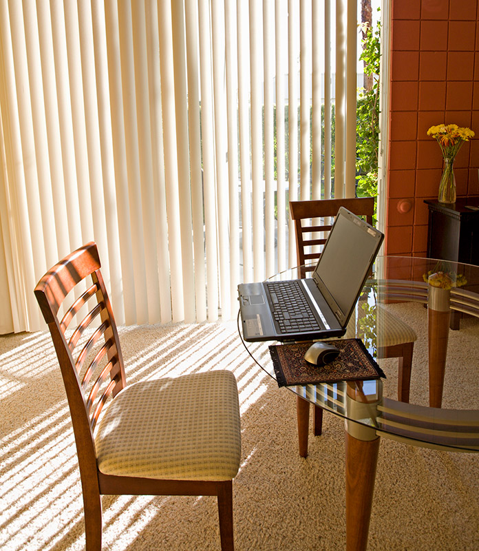 Vertical blinds by Oregon Blinds hang in front of a patio door in this home office